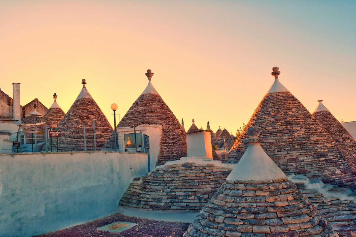 Scorcio panoramico dei trulli di Alberobello all'alba, vista dalla strada principale, atmosfera accogliente e invitante