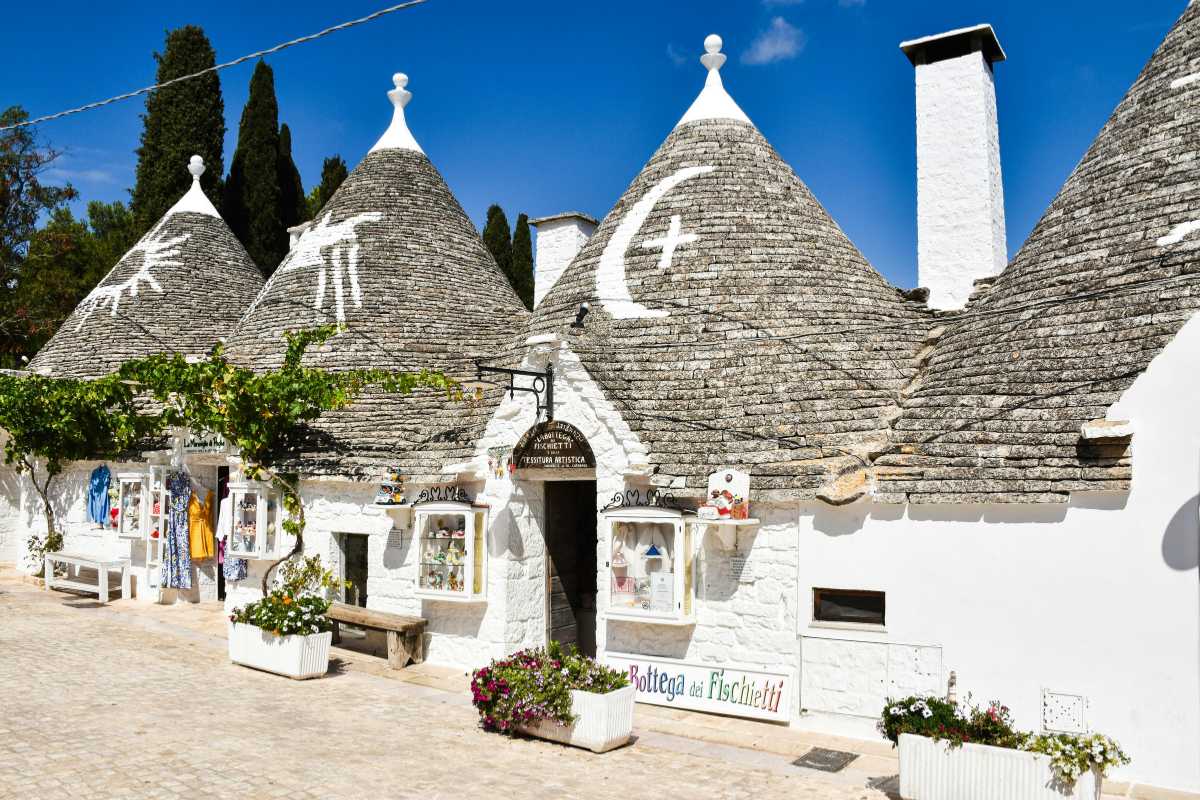 Vagone regionale della Ferrovia Sud Est in arrivo alla stazione di Alberobello, trulli visibili sullo sfondo, atmosfera rilassata