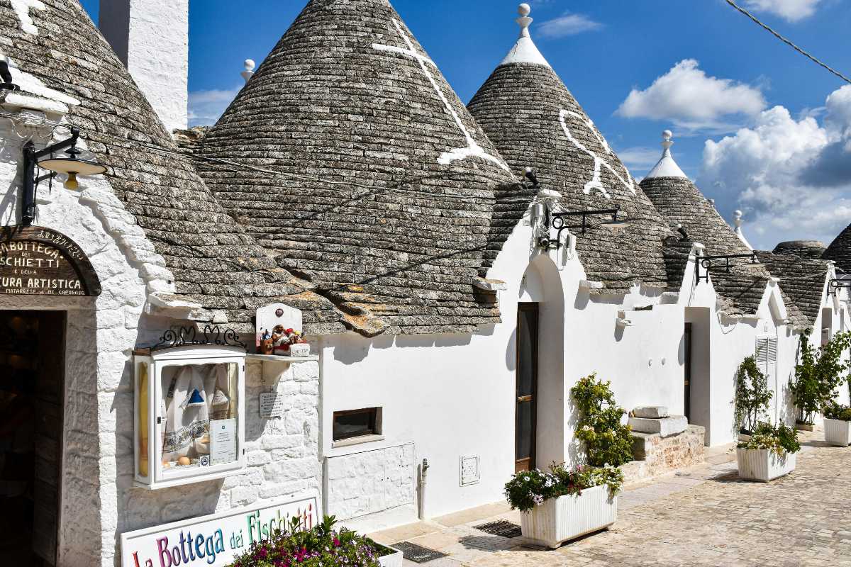 Panorama primaverile di un sentiero nel Bosco Selva di Alberobello con trulli sullo sfondo e famiglie in cammino